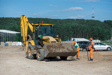 Industrial construction site of new commercial shopping mall. Excavator in front, concrete piles foundation for the building. Ongoing framing, construction of factory. Construction workers and trucks © lainen