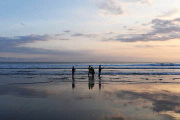 Silhouette group children fishing in ocean surf at sunset.