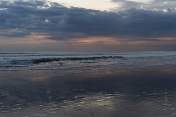 Nature in twilight period. Sunrise or sunset over the sea with tropical beach. Water and sky. Dark tone clouds.