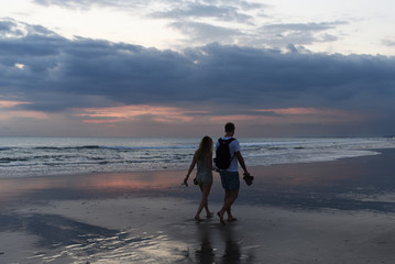 Silhouette romantic couple in love walking on the beach on bright  sunset background. Happy young couple  enjoying ocean sunset during travel.  People on summer beach holiday. Vacation concept.
