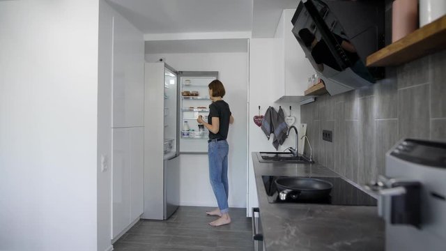 alone young woman is getting eggs from fridge in her kitchen in morning, preparing for cooking breakfast