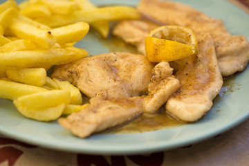 Freshly baked chicken fillet with french fries with lemon sauce on plate. Dinner is ready 
