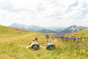  Pareja de excursionistas descansando tumbados en un hermoso prado mientras miran las nubes....