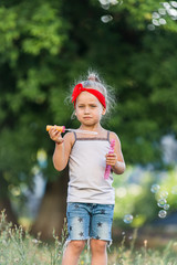 little girl is walking in the park and blowing soap bubbles