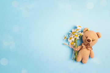 Cute toy bear with chamomile flowers and copy space on a blue background.