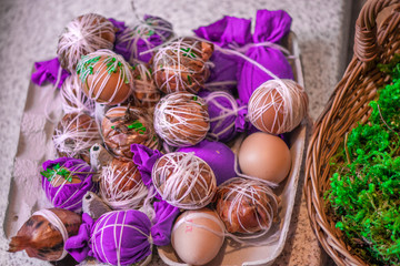 Easter eggs prepared for dyeing in onions peels, decorated with natural fresh leaves, plants, rice, colorful fabric and tied with white threads. Eggs laying in wicker wooden basket full of green grass