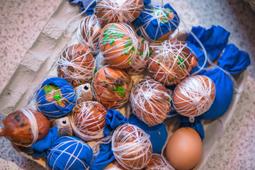 Fototapeta na wymiar Easter eggs prepared for dyeing in onions peels, decorated with natural fresh leaves, plants, rice, colorful fabric and tied with white threads. Eggs laying in wicker wooden basket full of green grass