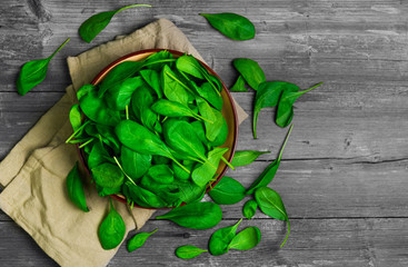 Fresh green leaves mini spinach in ceramic bowl. Spinach leaves on the gray wooden rustic background. Top view.