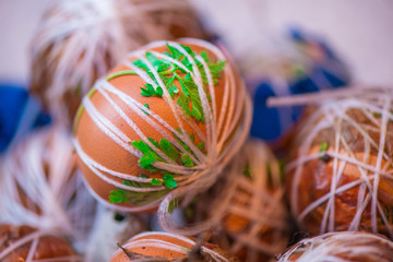 Easter eggs prepared for dyeing in onions peels, decorated with natural fresh leaves, plants, rice, colorful fabric and tied with white threads. Eggs laying in wicker wooden basket full of green grass