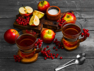Autumn tea drink (compote) from apples and berries of Kalina. Ingredients are sugar, calyx berries, fresh sliced apples. Rustic gray vintage background.