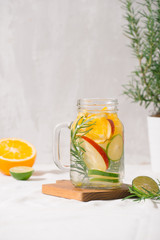 Detox water with lime, organe, apple and rosemary in a mason jar glass with a white wooden background