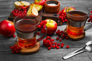 Autumn tea drink (compote) from apples and berries of Kalina. Ingredients are sugar, calyx berries, fresh sliced apples. Rustic gray vintage background.