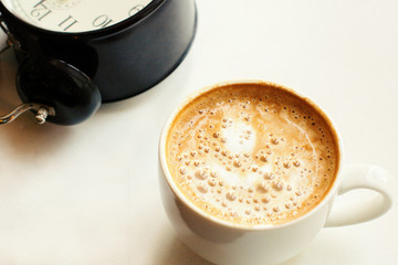 coffee in a white cup with a beautiful foam and black alarm clock