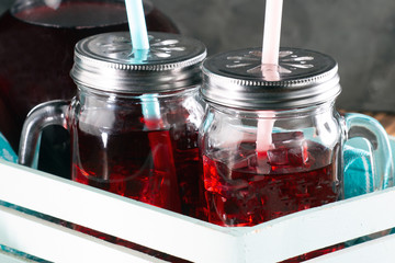 Pomegranate juice with ice in a decanter and a jar on a dark wooden background. Rustic style.