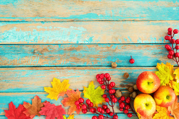 Apples and red berry on wooden table over maple leaves. Autumn background with copy space