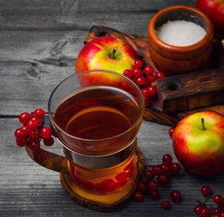 Autumn tea drink (compote) from apples and berries of Kalina. Ingredients are sugar, calyx berries, fresh sliced apples. Rustic gray vintage background.