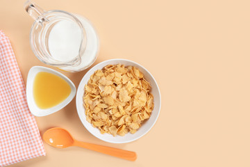 corn flakes in a bowl with jug of milk honey napkin and plastic spoon on orange background, copy space for text. quick breakfast for modern lifestyle concept.