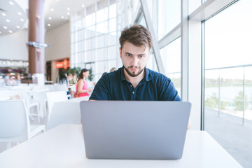Portrait of an attractive chelovek who is sitting with a laptop in a cafe and looking into the...