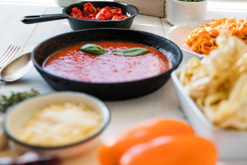 Italian food cooking concept. Ingredients for preparation pasta. Tomato, olive oil, spices, herbs, cheese, tomato sauce on a weathered wooden table indoors illuminated by the summer sun. Healthy food.