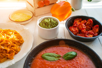 Italian food cooking concept. Ingredients for preparation pasta. Tomato, olive oil, spices, herbs, cheese, tomato sauce on a weathered wooden table indoors illuminated by the summer sun. Healthy food.