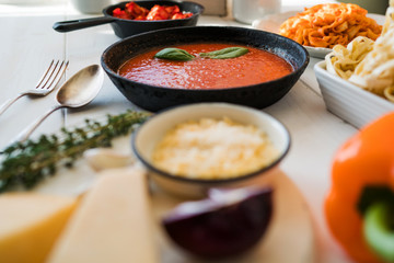 Italian food cooking concept. Ingredients for preparation pasta. Tomato, olive oil, spices, herbs, cheese, tomato sauce on a weathered wooden table indoors illuminated by the summer sun. Healthy food.