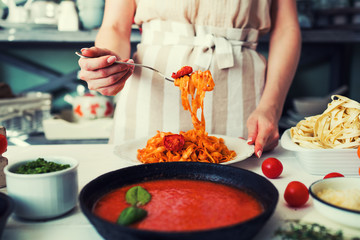 Italian style pasta dinner. Pasta with tomato and basil in plate on the wooden rustic table and ingredients for cooking. Chef hands preparing delicious pasta with tomato sous. Homemade food.