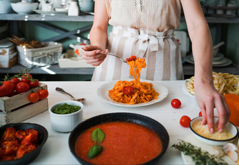 Italian style pasta dinner. Pasta with tomato and basil in plate on the wooden rustic table and ingredients for cooking. Chef hands preparing delicious pasta with tomato sous. Homemade food.