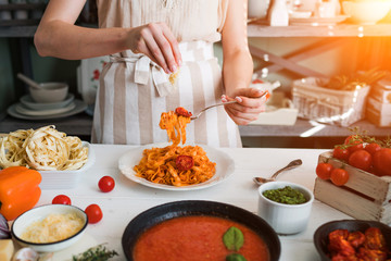 Italian style pasta dinner. Pasta with tomato and basil in plate on the wooden rustic table and ingredients for cooking. Chef hands preparing delicious pasta with tomato sous. Homemade food.