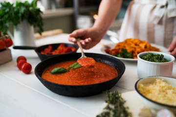 Food, family and people concept. Woman making homemade pasta for dinner at home kitchen. Pasta with ingredients. Tomatoes, garlic, parsley, pepper, and parmesan cheese on white wooden background.