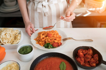 Woman making homemade pasta with tomato sous and cheese over old wooden table. Tomato, olive oil, spices, herbs, cheese, tomato sauce on a weathered wooden table in the summer sun's rays. Organic food