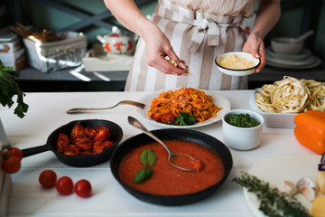 Food, family and people concept. Woman making homemade pasta for dinner at home kitchen. Pasta with ingredients. Tomatoes, garlic, parsley, pepper, and parmesan cheese on white wooden background.