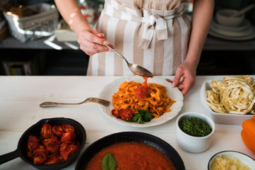 Food, family and people concept. Woman making homemade pasta for dinner at home kitchen. Pasta with ingredients. Tomatoes, garlic, parsley, pepper, and parmesan cheese on white wooden background.