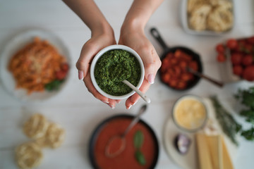 Woman holding small bowl with fresh homemade pesto. Cooking at home. Healthy organic food concept. Vegetarian vegetables, organic food, raw ingredient. Natural nutrition diet. Toned picture.