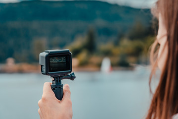 Young european woman filming with action camera lake and forest in the black forest