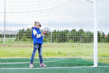 Little girl stands in the football gate as a goalkeeper and wants to catch the ball in her hands