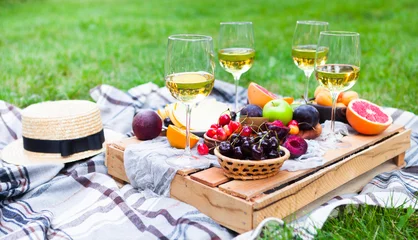 Foto auf Leinwand Picknickhintergrund mit Weißwein und Sommerfrüchten auf grünem Gras, Sommerparty © yatcenko