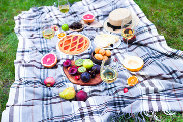 Picnic background with white wine and summer fruits on green grass, summertime party