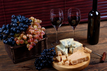 Danablu delicatessen cheese lying on platter near to red dry sauvignon in glasses standing on retro wooden table in rustic style for enjoyable dinner.