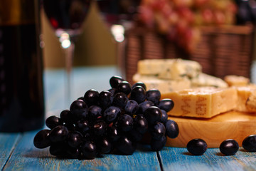 Obraz premium Closeup image of dark blue grape bunch lying on vintage table near to board with tasteful Roquefort slices for delicious degustation.