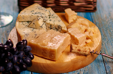 Closeup image of corkscrew, bunch of natural grape, delicateness brie slices lying on board.Healthy ripe fruit, tasty dairy food in rustic style.