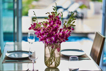 Bouquet of violet orchids in glass vase near the window, horizontal photo. Selective focus.
