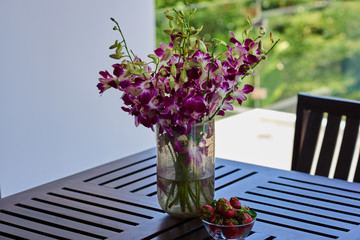 Glass vase with bouquet of beautiful violet orchids  in the garden background.