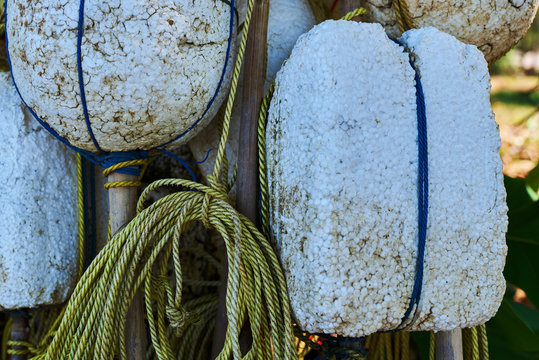 Fishing floats hanging on a wall outdoors. White foam plastic floats used for fishing with nets hanging with ropes. Abstract background with fishing buoys.