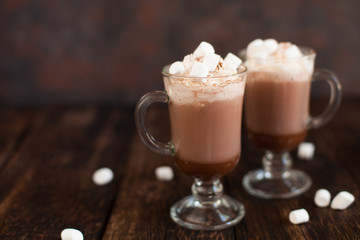 Two glasses with Hot chocolate garnished with whipped cream, marsmallow and cocoa powder.