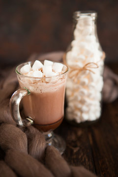 Two glasses with Hot chocolate garnished with whipped cream, marsmallow and cocoa powder on  wooden background with Cozy plaid from merinose wool