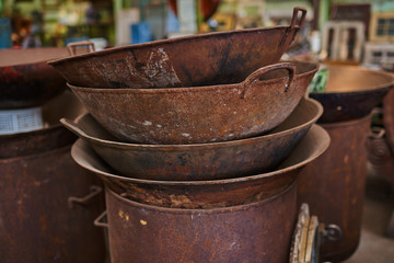 Stack of old rusty wok-pans. Retro equipment of cooking. Various objects for sale at indoor flea market. View of a display full of interesting old things for sale. Vintage assorted second-hand objects