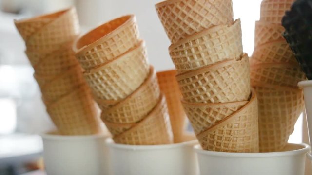 Empty fried waffle cones are stacked in each other. Real time, indoors, day, close-up, camera approaching object