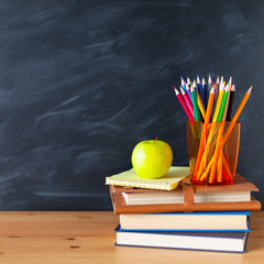 Back to School cocept. Still life with school books, pencils and apple against blackboard background