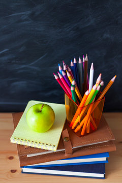 Back to School cocept. Still life with school books, pencils and apple against blackboard background