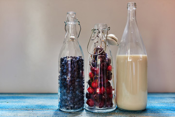 Three pitchers are on a wooden table in one poured milk in the other two falling asleep berries